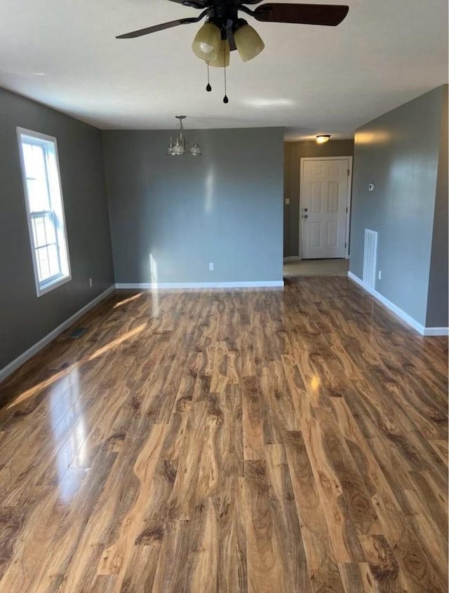 empty room featuring ceiling fan with notable chandelier, dark wood-style flooring, visible vents, and baseboards