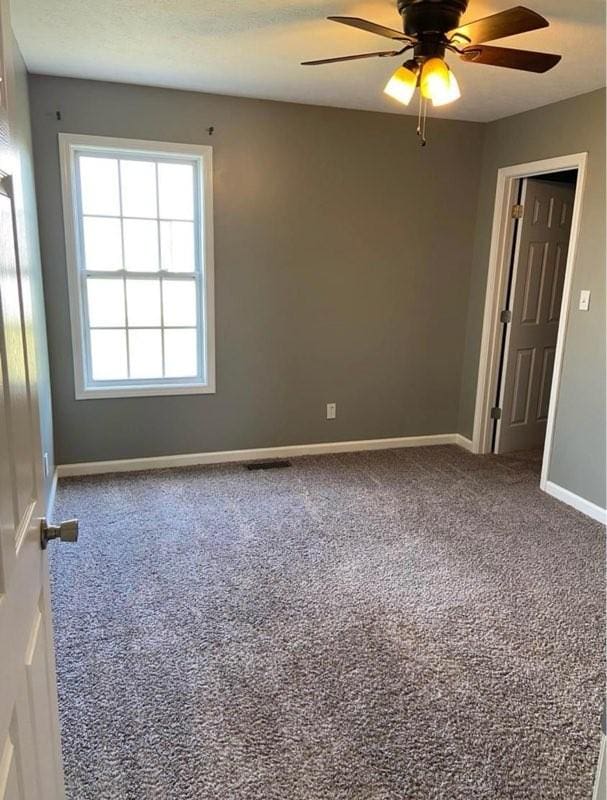 carpeted empty room with a textured ceiling, baseboards, and a ceiling fan