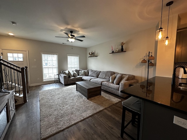 living area with dark wood-style floors, stairs, a ceiling fan, and baseboards