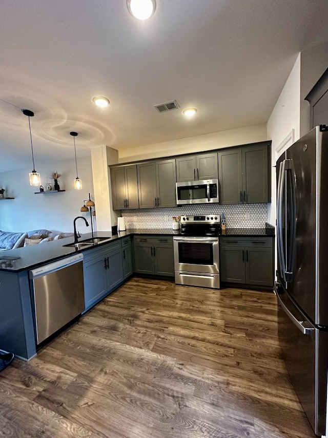 kitchen featuring stainless steel appliances, dark wood-type flooring, a sink, visible vents, and dark countertops