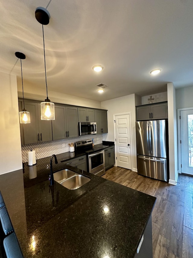 kitchen with decorative backsplash, dark wood-style flooring, a peninsula, stainless steel appliances, and a sink