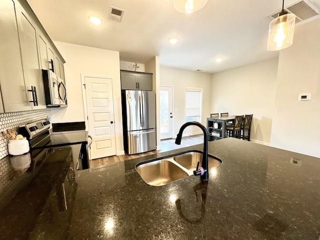 kitchen featuring appliances with stainless steel finishes, dark stone countertops, a sink, and visible vents