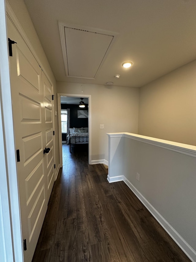 corridor with attic access, baseboards, dark wood-type flooring, and an upstairs landing