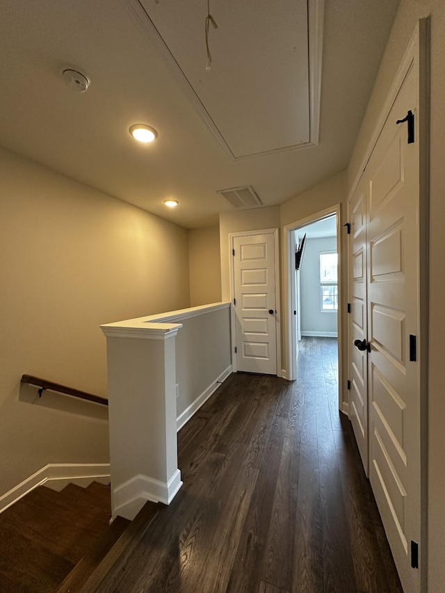 hall with dark wood-style flooring, visible vents, attic access, an upstairs landing, and baseboards