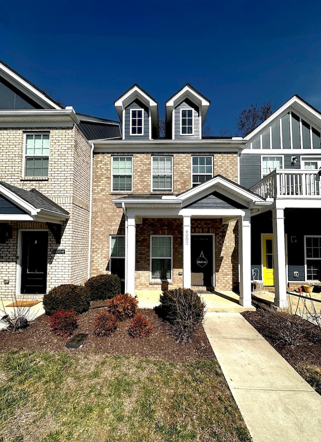 view of property with covered porch, brick siding, and a balcony