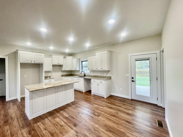 kitchen featuring a sink, wood finished floors, a kitchen island, visible vents, and white cabinets