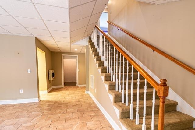 stairs featuring heating unit, baseboards, and a drop ceiling