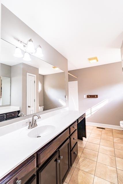 bathroom with visible vents, toilet, vanity, baseboards, and tile patterned floors