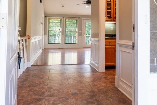 interior space featuring a ceiling fan, dark tile patterned flooring, a wainscoted wall, and a decorative wall