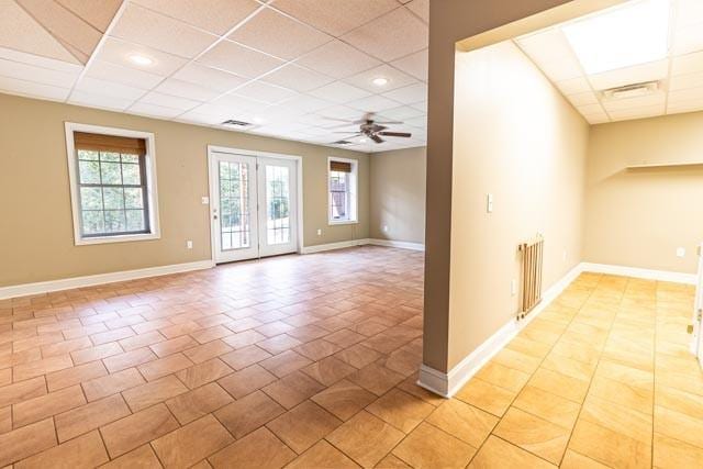 unfurnished room with a paneled ceiling, visible vents, radiator heating unit, a ceiling fan, and baseboards