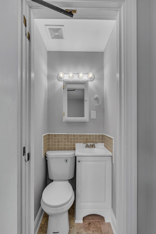 half bathroom with visible vents, toilet, a wainscoted wall, vanity, and tile walls