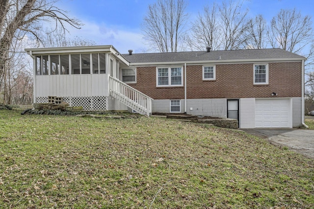 rear view of property featuring aphalt driveway, brick siding, a lawn, a sunroom, and a garage