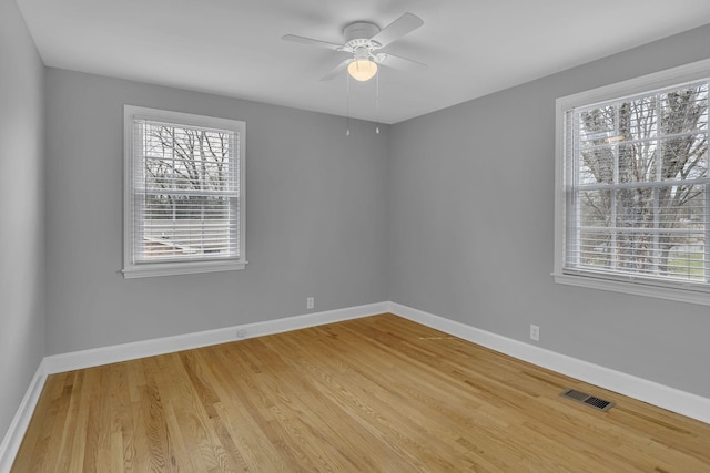 spare room featuring baseboards, light wood-style floors, visible vents, and a healthy amount of sunlight