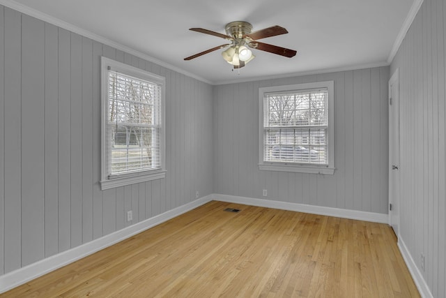 empty room featuring ceiling fan, visible vents, baseboards, light wood finished floors, and crown molding