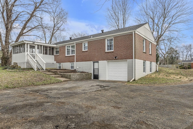 back of property featuring a sunroom, brick siding, driveway, and an attached garage