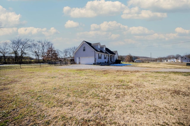 exterior space featuring driveway, an attached garage, fence, and a lawn