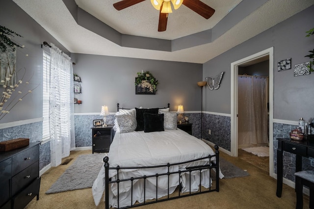 bedroom featuring carpet floors, a tray ceiling, a wainscoted wall, and a textured ceiling