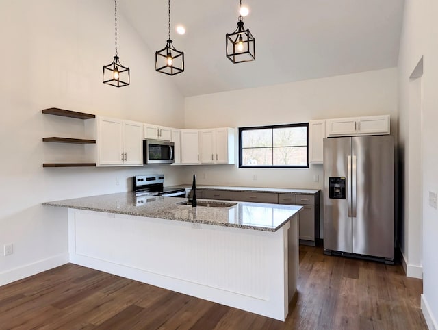 kitchen with appliances with stainless steel finishes, dark wood-style flooring, a peninsula, light stone countertops, and a sink