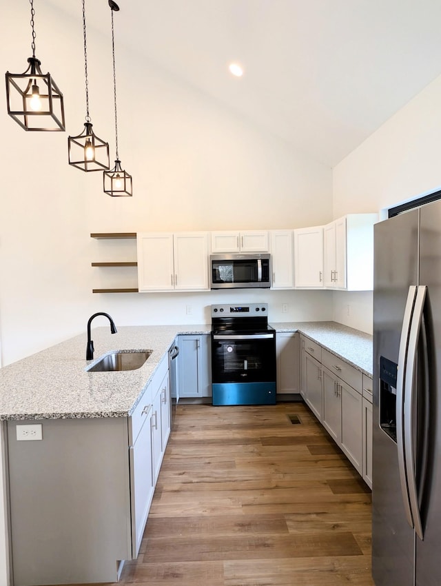 kitchen with decorative light fixtures, light wood finished floors, open shelves, stainless steel appliances, and a sink