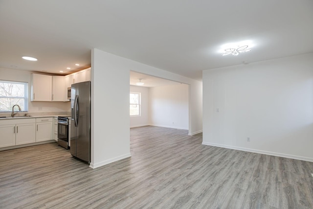 kitchen with light wood finished floors, light countertops, appliances with stainless steel finishes, open floor plan, and a sink