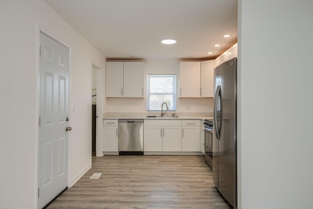 kitchen featuring a sink, white cabinetry, light wood-style floors, light countertops, and appliances with stainless steel finishes