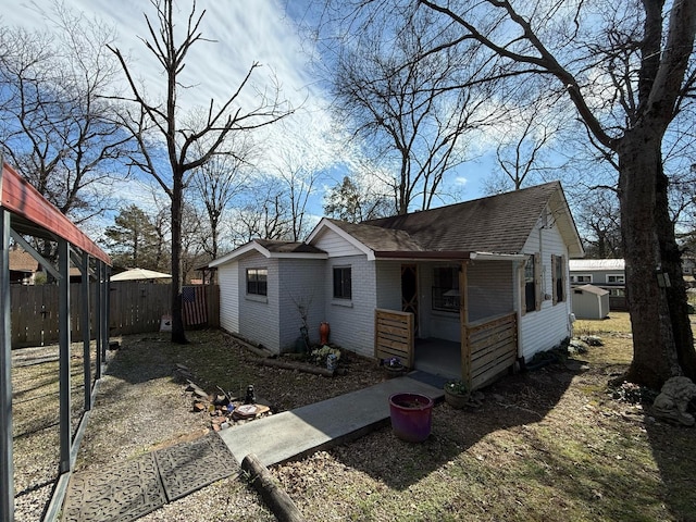 bungalow-style home featuring roof with shingles, fence, and brick siding