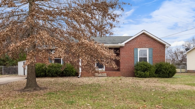 view of front facade with roof with shingles, a front yard, fence, and brick siding