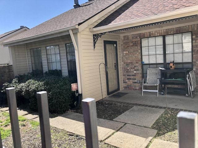 property entrance with a shingled roof and brick siding