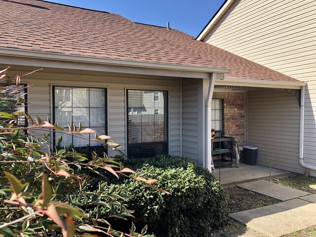 view of exterior entry with roof with shingles and brick siding