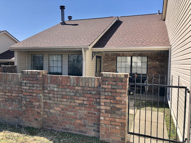 view of front of house with brick siding, a fenced front yard, a shingled roof, and a gate