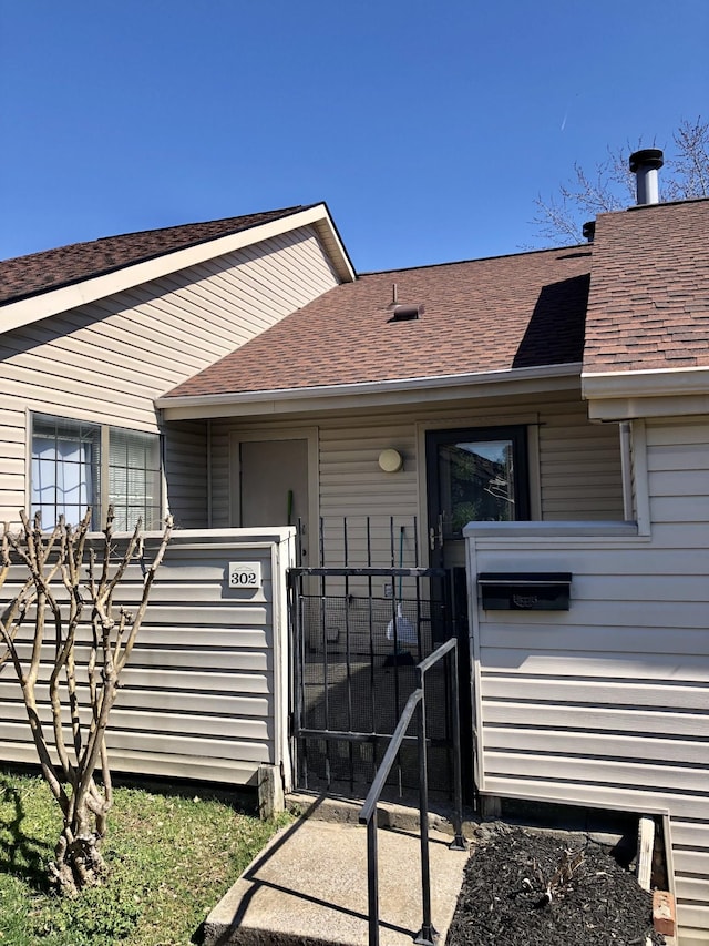 property entrance with a gate, fence, and roof with shingles