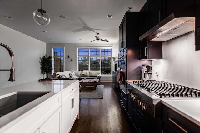 kitchen featuring open floor plan, oven, light countertops, under cabinet range hood, and a sink