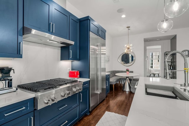 kitchen featuring blue cabinetry, stainless steel appliances, light countertops, a sink, and under cabinet range hood