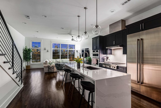 kitchen with a kitchen island with sink, stainless steel appliances, a sink, visible vents, and dark cabinetry