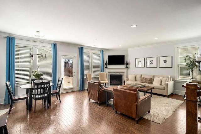 living area featuring baseboards, ornamental molding, dark wood-type flooring, an inviting chandelier, and a fireplace