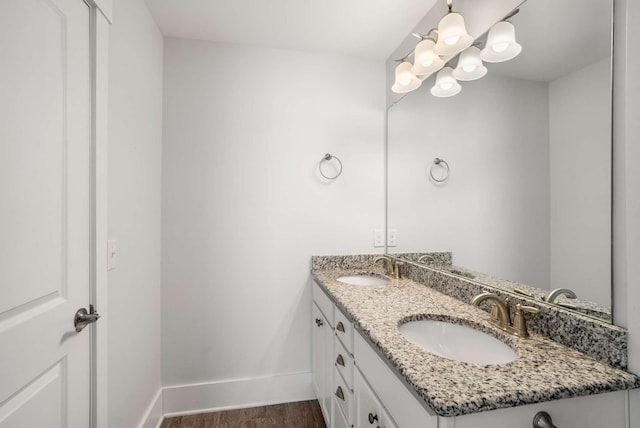 bathroom with double vanity, baseboards, a sink, and wood finished floors