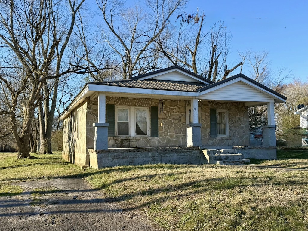 bungalow featuring a porch, stone siding, metal roof, and a front lawn