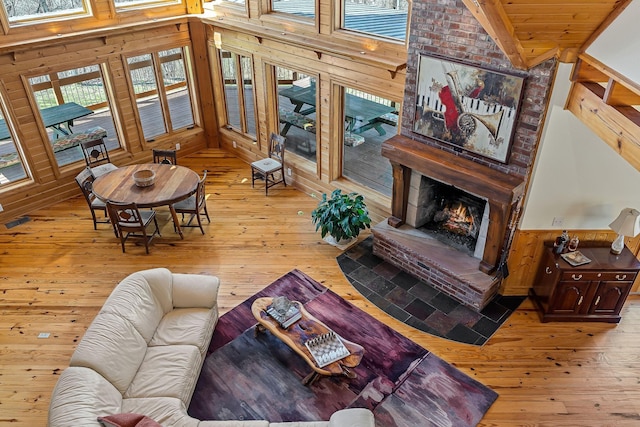 living area featuring high vaulted ceiling, wooden walls, a fireplace, wainscoting, and wood-type flooring