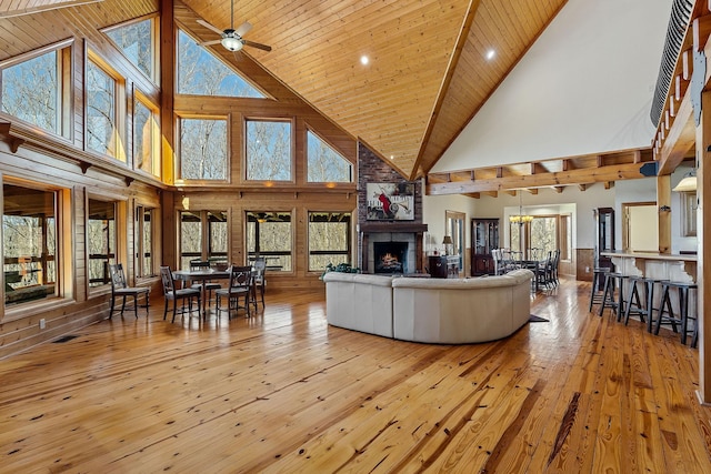 living area featuring lofted ceiling, a ceiling fan, wood ceiling, a large fireplace, and hardwood / wood-style flooring