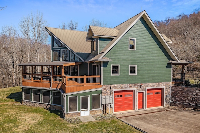 rear view of house featuring a yard, concrete driveway, metal roof, a garage, and stone siding