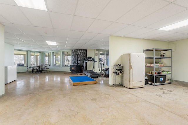 exercise room with a paneled ceiling, a wood stove, and baseboards