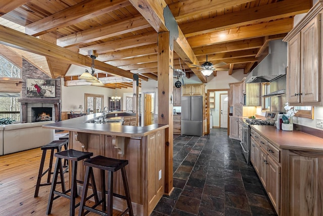 kitchen featuring wall chimney range hood, wood ceiling, a large fireplace, and stainless steel appliances