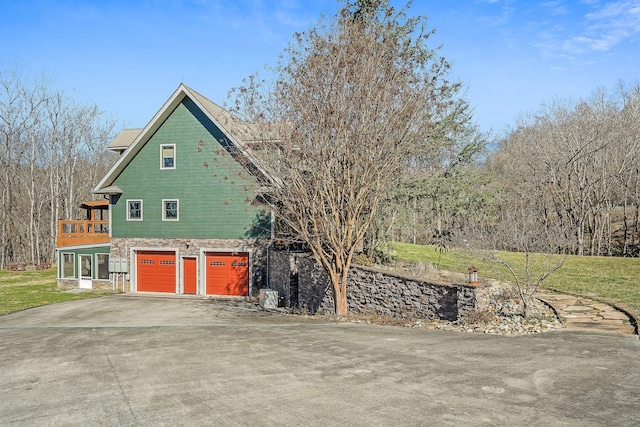 view of side of home featuring aphalt driveway, stone siding, a yard, and a garage