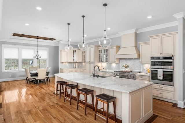 kitchen featuring light wood finished floors, custom range hood, ornamental molding, stainless steel appliances, and a sink