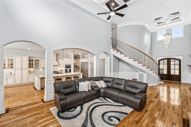 living room with french doors, crown molding, stairway, a towering ceiling, and light wood-type flooring