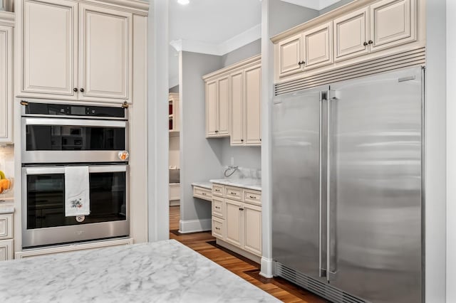 kitchen with ornamental molding, appliances with stainless steel finishes, dark wood-style floors, and cream cabinetry