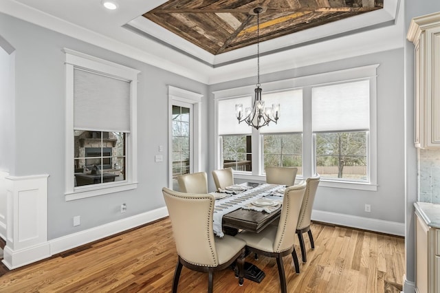 dining area featuring light wood-style flooring, a tray ceiling, a chandelier, and baseboards