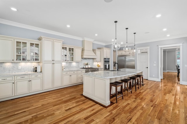 kitchen featuring light wood finished floors, appliances with stainless steel finishes, a kitchen breakfast bar, premium range hood, and a sink