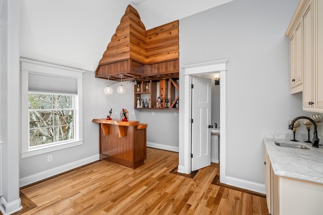 kitchen with cream cabinetry, light wood-style flooring, a sink, light stone countertops, and baseboards