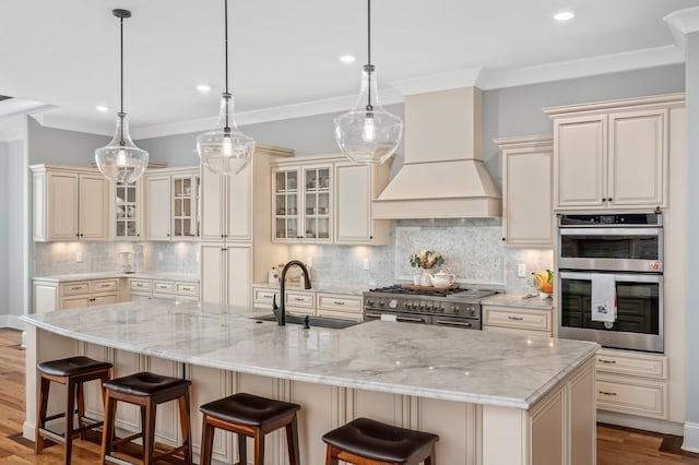 kitchen with stainless steel appliances, a sink, cream cabinetry, ornamental molding, and custom exhaust hood